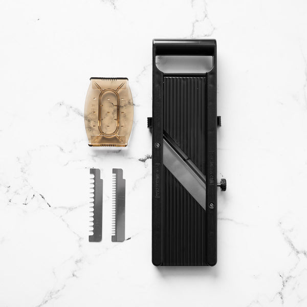 A black mandoline slicer with an interchangeable blade attachment and two guide blades, arranged on a white marble background.